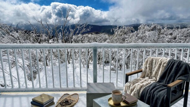 A balcony with a view of snow-covered trees and mountains, a chair with a blanket, and a table with books and a cup. - Matterhorn Chalet –Mount Buller Alpine Chalet. Mountain Views. Sleeps 12 (Mount Buller)