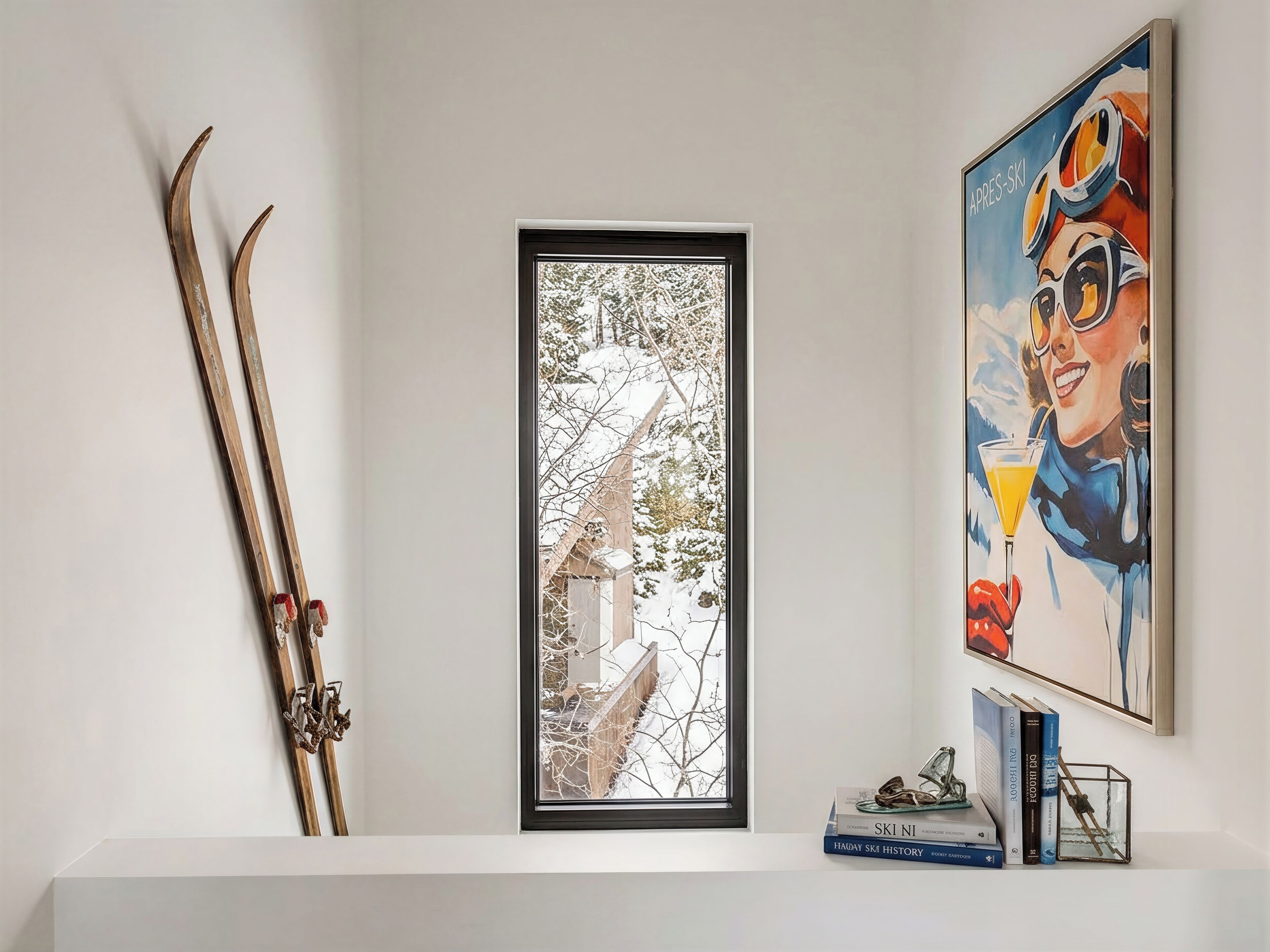 A framed photograph of a snowy landscape, a pair of skis leaning against the wall, and a colorful painting of a skier.