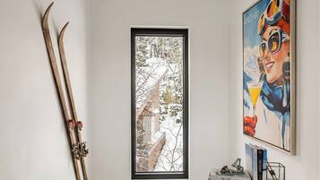 A framed photograph of a snowy landscape, a pair of skis leaning against the wall, and a colorful painting of a skier.