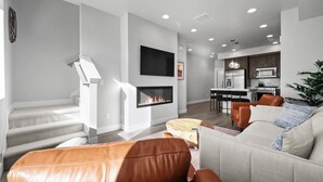 A modern living room with a fireplace, a sofa, and a dining area with a kitchen in the background. - Luxury 3 bed / 3 bath townhome in Park City, Sauna, 10 min to world-class skiing (Park City)