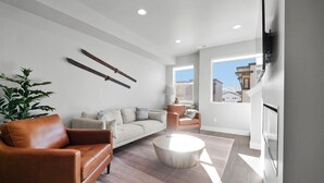 A modern living room with a leather sofa, a round coffee table, and a large window offering a view of buildings and mountains. - Luxury 3 bed / 3 bath townhome in Park City, Sauna, 10 min to world-class skiing (Park City)
