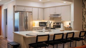 A modern kitchen with white cabinets, stainless steel appliances, a central island with bar stools, and a microwave. - River Run Retreat - Cowboy Pool, Fire Pit & Pool Table! Close to Campus & River (San Marcos)