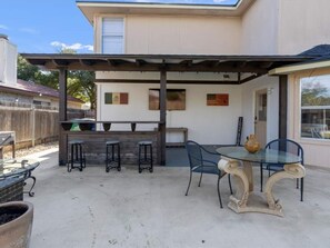 Rustic wooden bar with seating, a glass-top dining table, and an outdoor TV setup for game days. - Spacious & Stylish 4 BR house Round Rock (Round Rock)