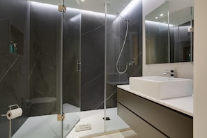 A modern bathroom with a glass-enclosed shower, a white sink, and a marble-tiled wall.
