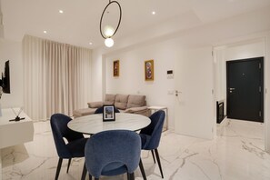 A modern dining area with a round table, blue chairs, a sofa, and a black door.