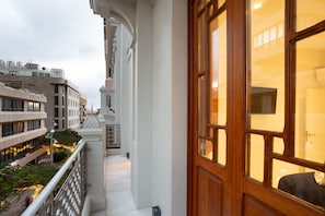 Un balcón con vista a la ciudad, una puerta de madera y una barandilla blanca.