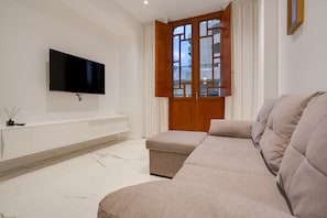 A modern living room with a flat-screen TV, a sofa, a cabinet, and a wooden door with glass panels.