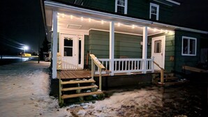 Una casa verde con un porche, escalones y luces colgantes.