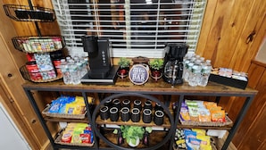 Una estación de café con cafetera, botellas de agua, snacks y un cartel que dice 'The Coffee Bar'.