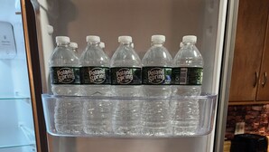 Un refrigerador con varios estantes llenos de botellas de agua Poland Spring.
