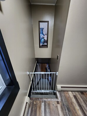 Una escalera estrecha con barandilla blanca, paredes color beige y una obra de arte enmarcada en la parte superior.