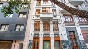 Ein mehrgeschossiges Gebäude mit einem markanten Eingang, großen Fenstern und einem Balkon mit Metallgeländern.