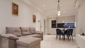Ein modernes Wohnzimmer mit einer Eckcouch, einem Essbereich mit Tisch und Stühlen sowie einer Küche mit Schränken und Geräten.