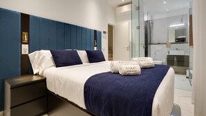Ein modernes Hotelzimmer mit Bett, Nachttisch, Duschkabine und Badezimmer mit Waschbecken und Spiegel.