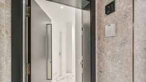 Ein modernes Interieur mit Glastür, Marmorboden und einem wandmontierten Bedienfeld für den Aufzug.