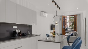 Una cocina moderna con una isla central, un comedor con sillas azules y vistas a través de un ventanal.