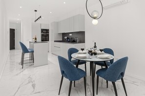 A modern kitchen with white cabinets, a dining area with a round table and blue chairs, and a bar area with a bottle of champagne.
