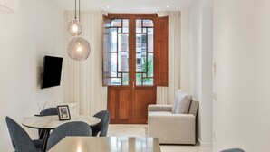 Una sala de estar moderna con comedor, televisor montado en la pared y una puerta grande de madera con paneles de vidrio.
