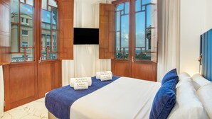 Habitación de hotel con cama, armario de madera, televisión y ventanas amplias.