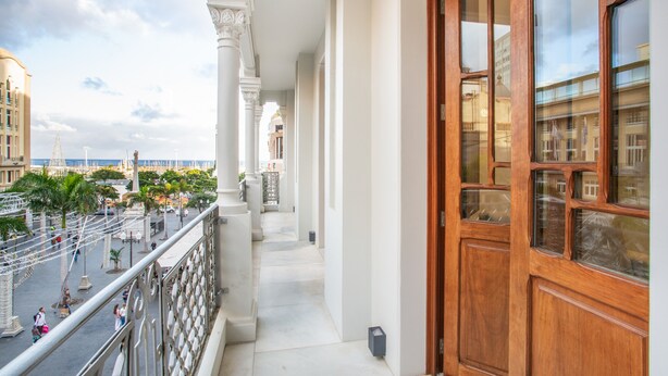 Un balcón con vistas a una plaza pública, una puerta de madera y columnas blancas.