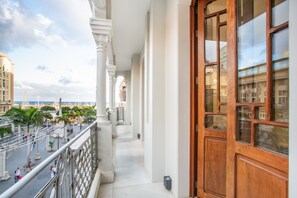Un balcon donnant sur une place publique, une porte en bois et des colonnes blanches.