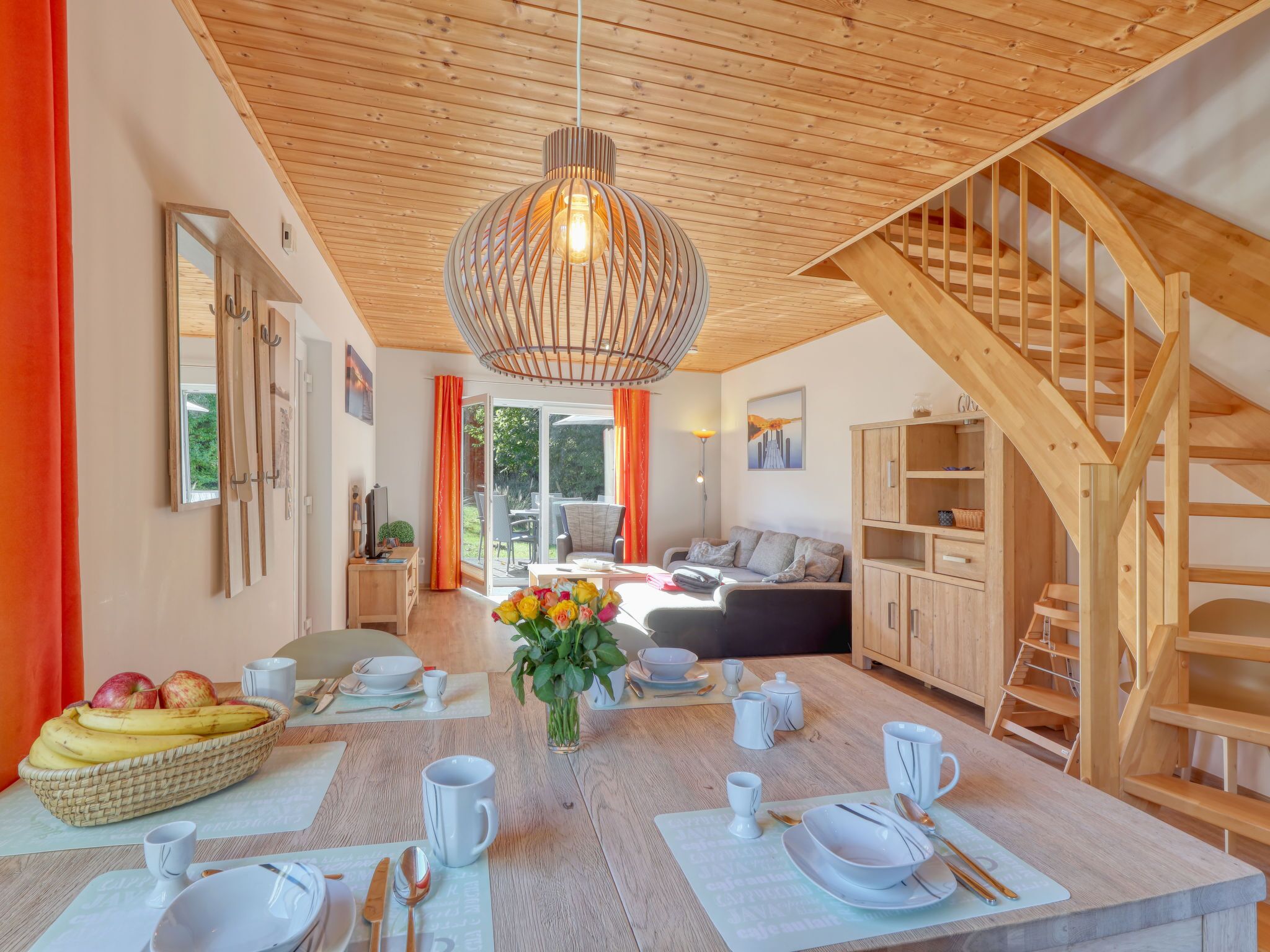Un soggiorno moderno con soffitto in legno, un'area pranzo con tavolo imbandito per quattro persone e una scala che conduce a un livello superiore.