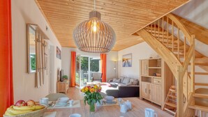 A modern living room with a wooden ceiling, a dining area with a table set for four, and a staircase leading to an upper level. - Strandläufer by Interhome (Seebad Altefähr)