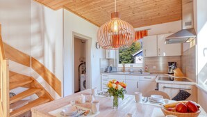 A modern kitchen with wooden beams, a hanging light fixture, and a dining area with a table set for two. - Strandläufer by Interhome (Seebad Altefähr)