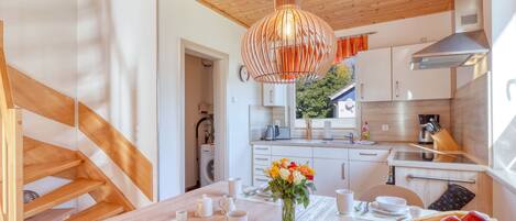 A modern kitchen with wooden beams, a hanging light fixture, and a dining area with a table set for two.