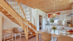 A modern kitchen with wooden accents, a dining area with a table set for two, and a wooden staircase. - Strandläufer by Interhome (Seebad Altefähr)