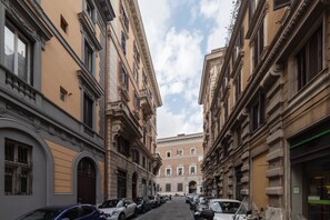 A cobblestone street lined with historic buildings, parked cars, and a clear sky.