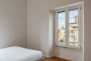 Ein Schlafzimmer mit einem Bett, einem großen Fenster mit Blick auf Gebäude und einem Holzboden.