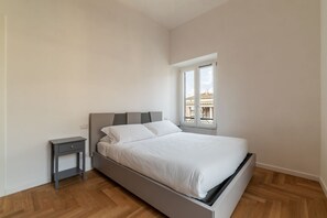 A bedroom with a bed, a nightstand, and a window with a view of buildings. - Vaccinari al Ghetto - FromHometoRome (Roma)