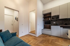 A modern kitchen with built-in appliances, a flat-screen TV, and a wooden herringboard floor.