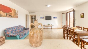 A living room with a sofa, a large vase, a dining table with chairs, and a television on the wall. - Villa 'La  -  Liscedde' with Sea View, Wi-Fi and Air Conditioning (Castrignano del capo)