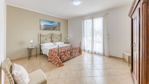 A bedroom with a bed, a nightstand, a chair, a wooden wardrobe, and a painting on the wall. - Villa 'La  -  Liscedde' with Sea View, Wi-Fi and Air Conditioning (Castrignano del capo)