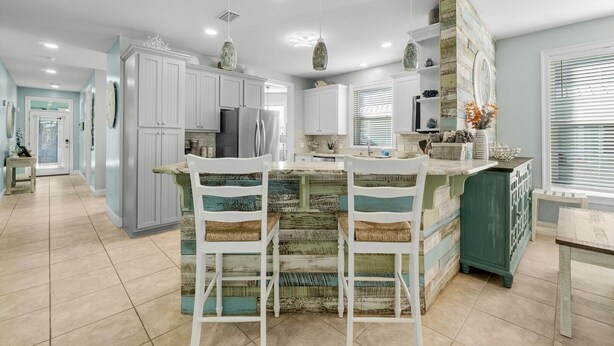 Una cocina amplia con una isla central, armarios blancos e iluminación colgante.