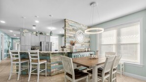 Una cocina moderna con armarios blancos, una isla de madera y un comedor con sillas blancas.
