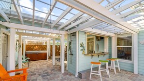 Un solárium con techo de vidrio, una bañera de hidromasaje y una zona de bar con taburetes.