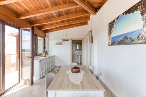 Un coin repas avec une table en bois, des chaises et une vue sur la mer, visible à travers une grande fenêtre.
