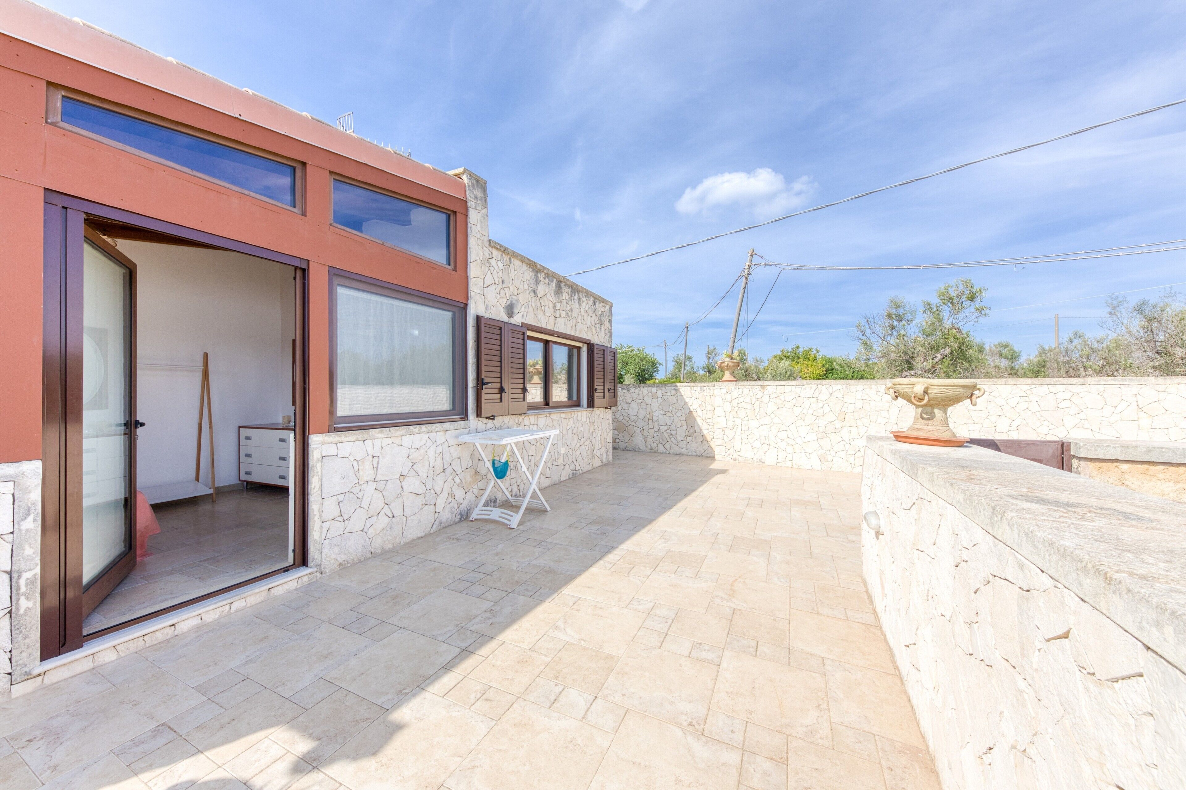 A modern building with a stone facade, large windows, and a patio area with a table and chairs.