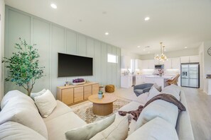 Una sala de estar moderna con un televisor de pantalla plana grande, un mueble de madera y un comedor con una cocina al fondo.
