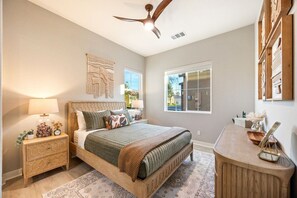 A bedroom with a bed, nightstands, a desk, a ceiling fan, and a large window.