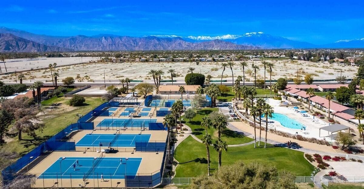 An aerial view of a resort with multiple tennis courts, a swimming pool, and a mountainous backdrop.