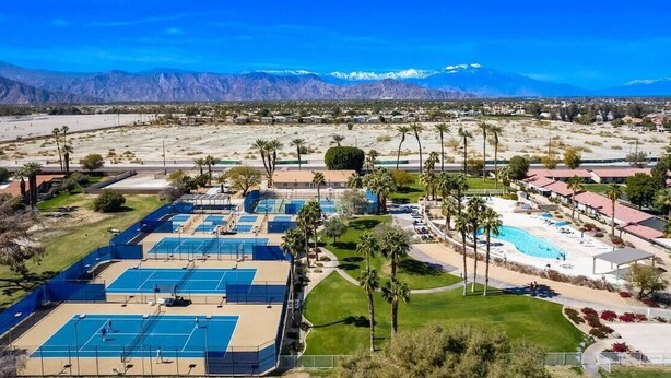 An aerial view of a resort with multiple tennis courts, a swimming pool, and a mountainous backdrop. - Fairway Gem: Pool+Spa, Putting Green, EV Charger! (Indio)