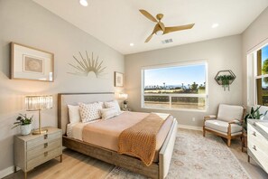 Une chambre à coucher comprenant un lit, des tables de chevet, un ventilateur de plafond, une fenêtre avec vue et un fauteuil.