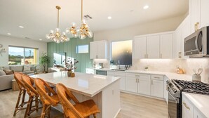 A modern kitchen with white cabinets, a central island with chairs, a gas stove, and pendant lighting. - Fairway Gem: Pool+Spa, Putting Green, EV Charger! (Indio)