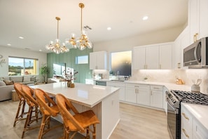 A modern kitchen with white cabinets, a central island with chairs, a gas stove, and pendant lighting. - Fairway Gem: Pool+Spa, Putting Green, EV Charger! (Indio)