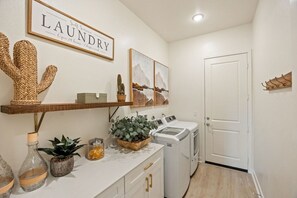 A laundry area with a self-service sign, a cactus decoration, a wooden shelf, a potted plant, and a washing machine.