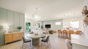 A modern kitchen with a dining area, a large chandelier, and a flat-screen TV. - Fairway Gem: Pool+Spa, Putting Green, EV Charger! (Indio)